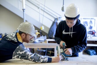 Geometry teacher Brian Hancock, left, helps sophomore De’Andre Saunders, 16, cut plywood for a tiny house on Friday, March 22, 2019 at Battle High School in Columbia, Mo. Students in a combined construction and geometry class are building a tiny house for a low-income family in the community.