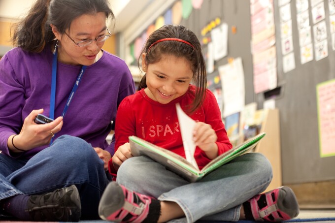 Teacher and student on the floor of a classroom reading a book.
