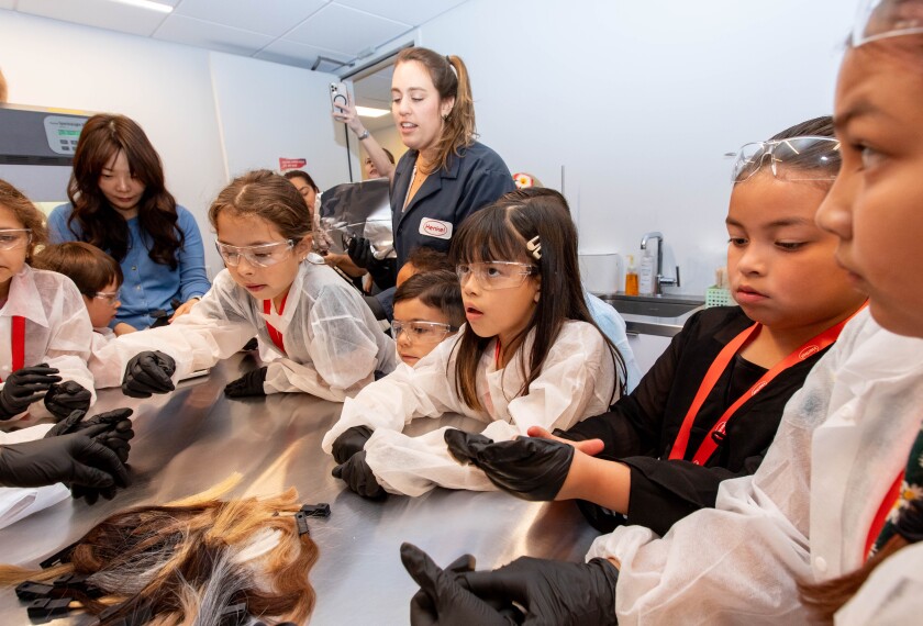 Youth students in a lab classroom examining hair extensions with Henkel instructors supervision