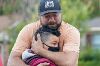 Russell Rakestraw II hugs his son, fourth grader Russell Rakestraw III, in front of his elementary school while dropping off on the first day of classes in Richardson, Texas, Tuesday, Aug. 17, 2021. Despite Texas Gov Greg Abbott's executive order banning mask mandates by local officials, the Richardson Independent School District and many others across the state are requiring masks for students.