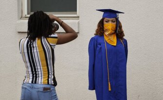 Anderson High School senior Teyaja Jones, right, poses in her cap and gown with a bandana face cover, Tuesday, May 5, 2020, in Austin, Texas. Texas’ stay-at-home orders due to the COVID-19 pandemic have expired and Texas Gov. Greg Abbott has eased restrictions on many businesses that have now opened, but school buildings remain closed.