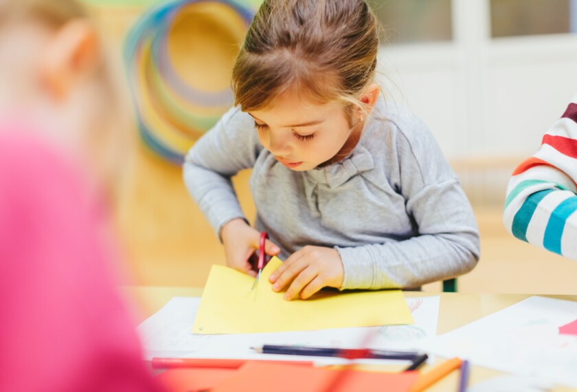 Young girl using scissors in classroom.
