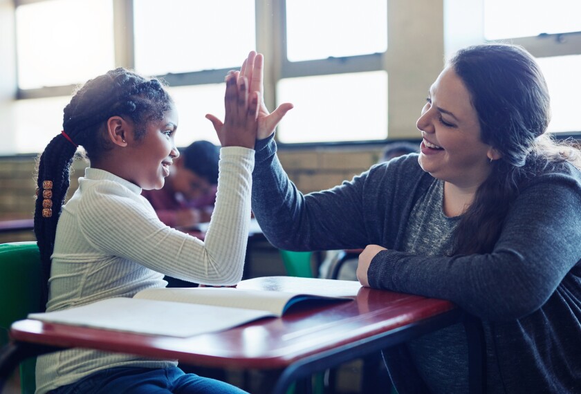 Young Black girl giving her teacher a high five in a classroom.