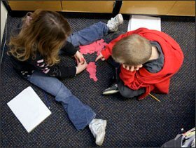 Working together, Mackenzie Bright and Caleb Holm sit on the floor with paper cutouts to solve math problems.
