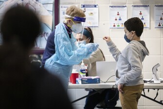 Peggy Donahue, a nurse at McGlynn Middle School, hands a student a q-tip to perform a self-administered COVID-19 test at McGlynn Middle School in Medford, Mass., on March 15, 2021.