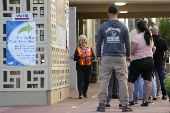 A poll worker talks with people in line to vote in the midterm election at the John F. Kennedy Library, Tuesday, Nov. 8, 2022, in Hialeah, Fla.