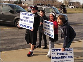 Students hold signs in favor of opting out of state assessments during a visit by New York’s education commissioner, MaryEllen Elia, to the William Street School in Lancaster.
