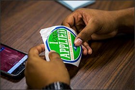 Senior Chance Macias signs a sticker to signify that he's finished his college application. Applicants' stickers are displayed on a wall at Northwest High School.